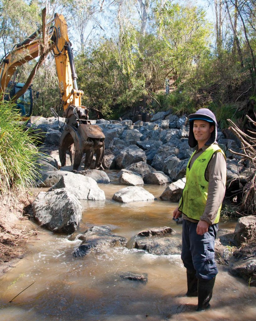 Matt Moore from Catchment Solutions in Mackay on a riverbed with rocks.